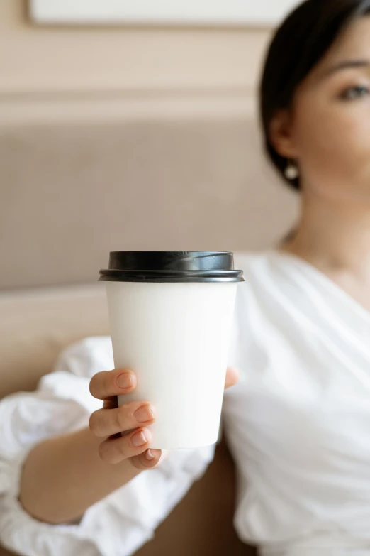 a woman sitting on a couch holding a cup of coffee, trending on pexels, minimalism, close up half body shot, avatar image, paper cup, soft blur