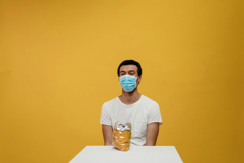 a man sitting at a table with a doughnut in front of him, an album cover, by Adam Marczyński, pexels contest winner, hyperrealism, medical mask, yellow hue, portrait of tall, beer