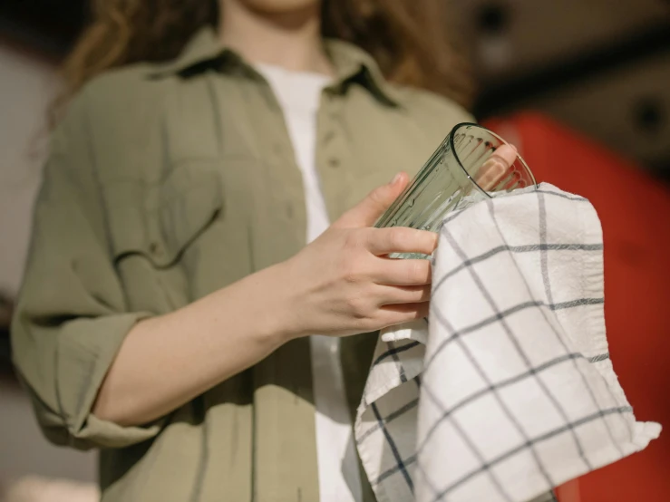 a woman holding a glass and a towel, by Nina Hamnett, trending on pexels, working clothes, glass jar, long flowing fabric, low quality photo