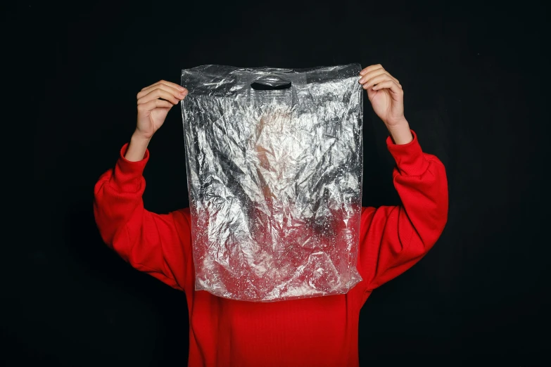 a person holding a plastic bag over their head, by Julia Pishtar, pexels contest winner, plasticien, silver red, wearing a shirt, tin foiling, official product photo