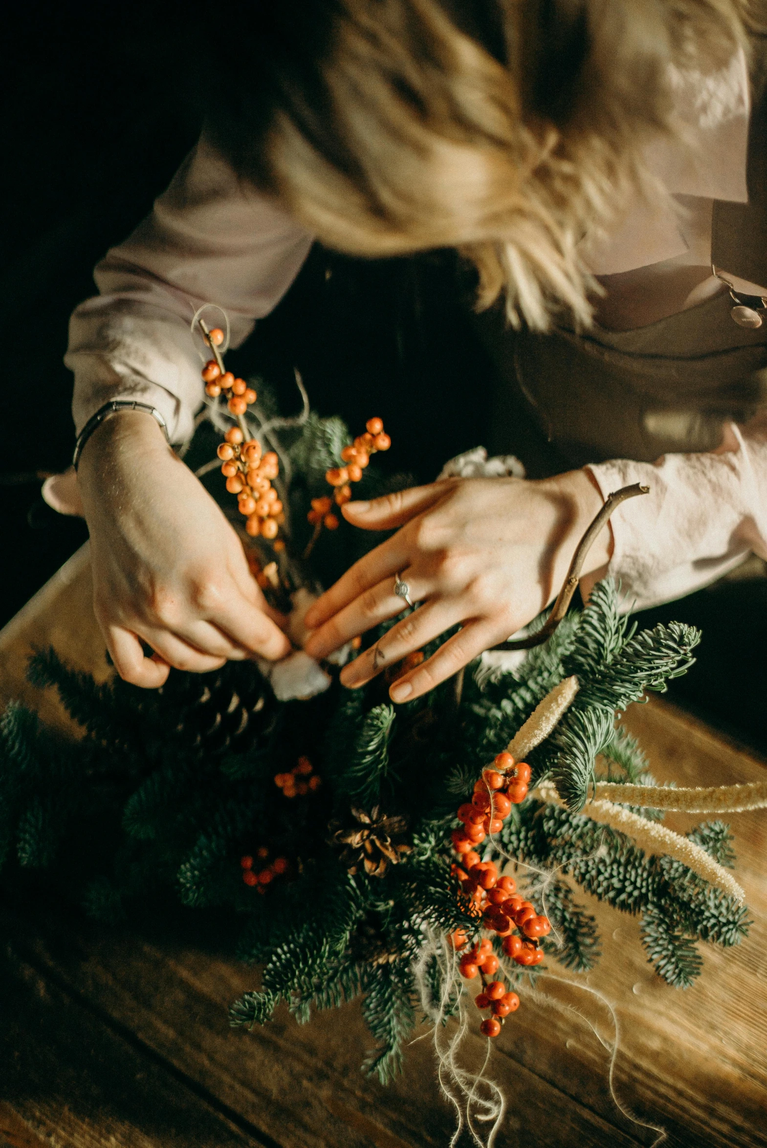 a woman arranging a christmas wreath on a table, by Sara Saftleven, trending on pexels, made of flowers and berries, branches wrapped, carving, close to night