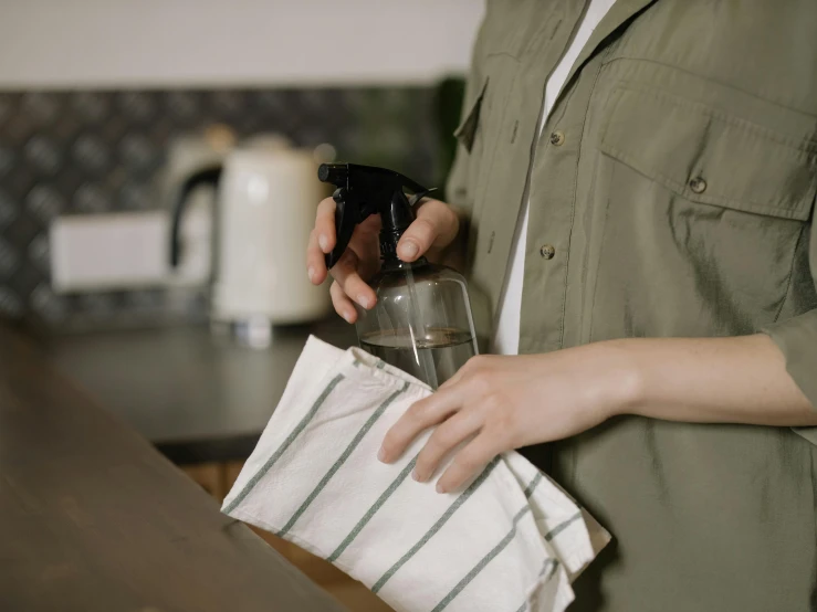 a close up of a person holding a spray bottle, a picture, transparent cloth, in a kitchen, profile image, brown