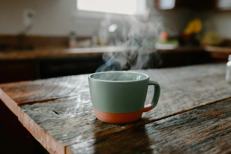 a cup sitting on top of a wooden table, by Jessie Algie, pexels contest winner, light green mist, cooking it up, grey, angled shot