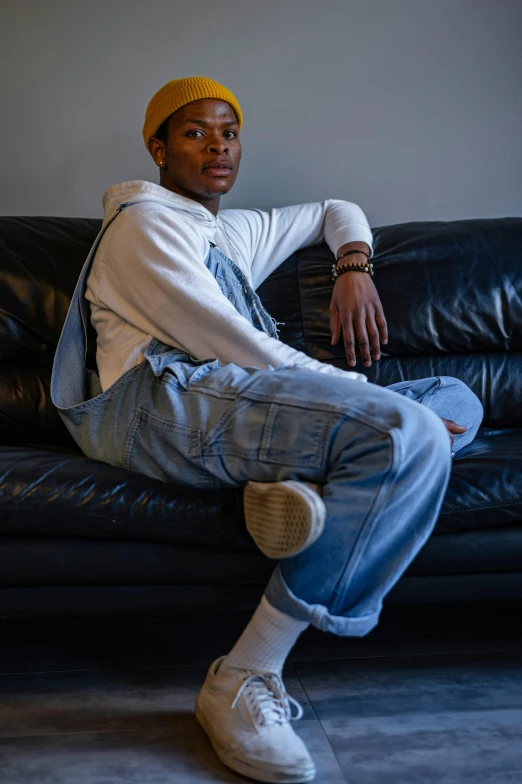 a man sitting on top of a black leather couch, by Thomas Furlong, trending on pexels, wearing blue jean overalls, non binary model, riyahd cassiem, androgynous person