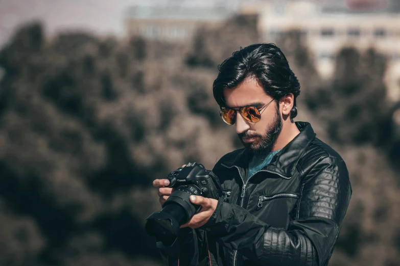 a man in a leather jacket holding a camera, by Ismail Acar, pexels contest winner, wearing oakley sunglasses, shabab alizadeh, profile picture 1024px, fan favorite