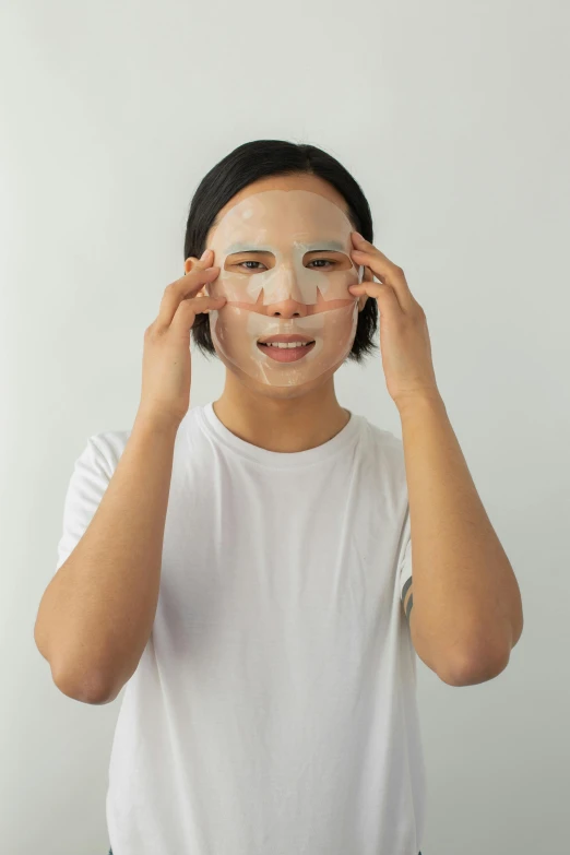 a woman putting a face mask on her face, ready to model, wearing translucent sheet, showing forehead, asian features