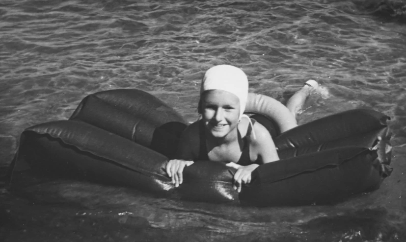a woman laying on an inflatable mattress in the water, a black and white photo, art deco, smiling into the camera, olympics event 1930's, teenage girl, amanda lilleston