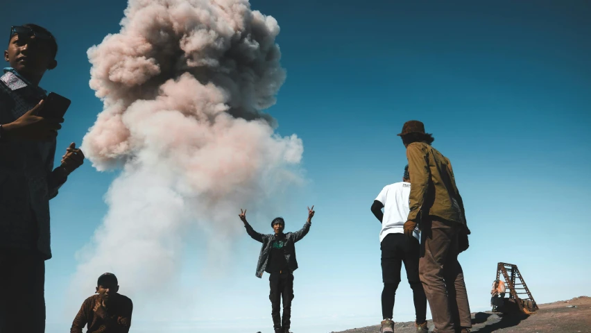 a group of people standing on top of a hill, by Niko Henrichon, pexels contest winner, happening, explosions and smoke, avatar image, men look up at the sky, volcanic workshop background