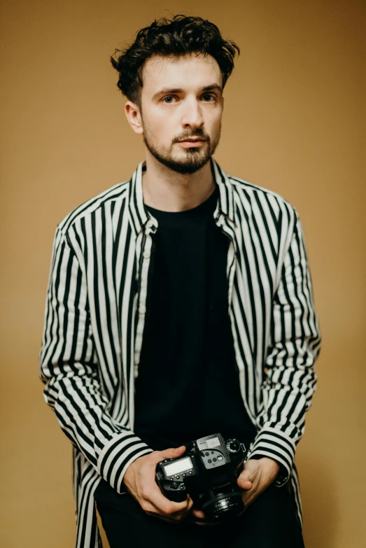 a man holding a camera in his hands, inspired by Dan Smith, striped shirt, studio photoshoot, liam, official photo