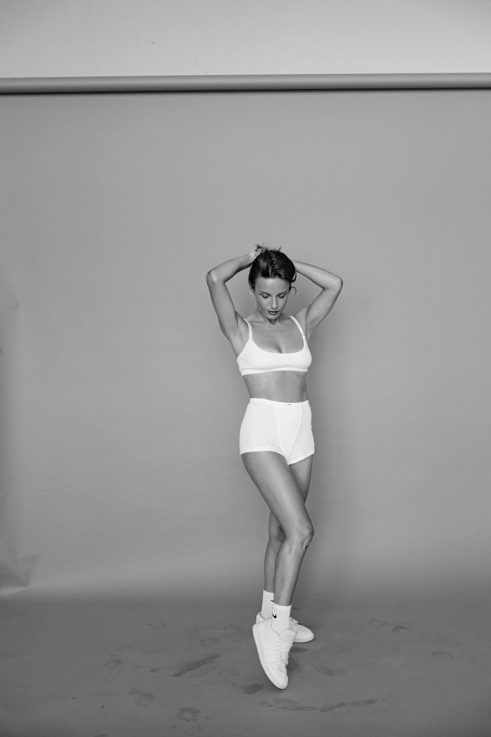 a black and white photo of a woman posing for a picture, a black and white photo, by Clifford Ross, dribble, wearing white leotard, bra and shorts streetwear, kate beckinsale, concept photoset