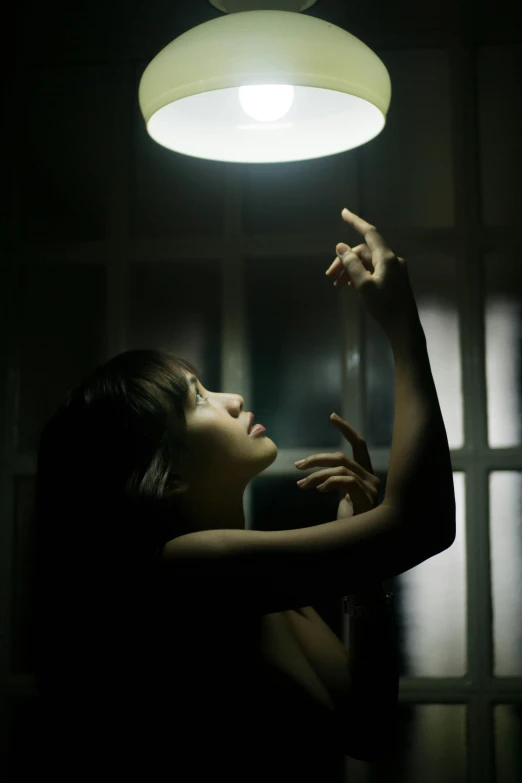a woman reaching up to a light in a dark room, asian woman, dark and foreboding