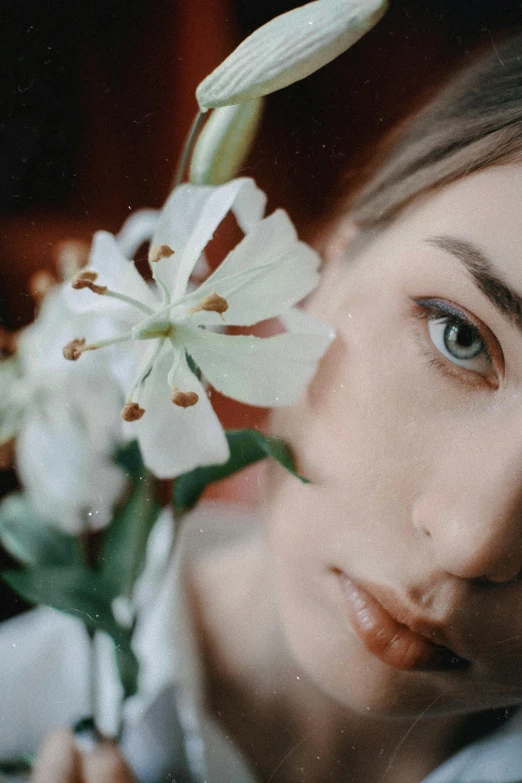 a close up of a person holding a flower, inspired by Elsa Bleda, trending on pexels, photorealism, white lilies, attractive face, anna nikonova aka newmilky, looks at the camera