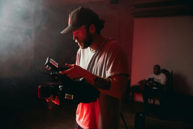 a man standing in a room holding a camera, red and cinematic lighting, performing a music video, avatar image, zachary corzine