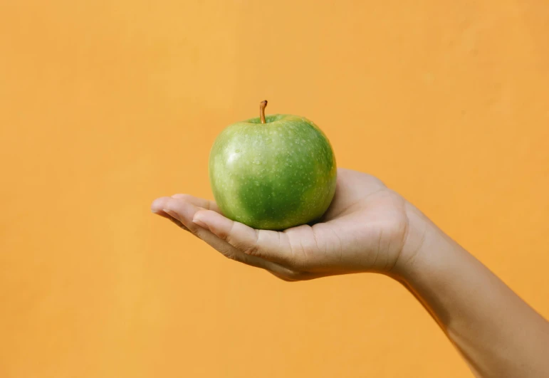 a person holding a green apple in their hand, by Emma Andijewska, pexels contest winner, background image, apple orange, plain background, holding a 🛡 and an 🪓