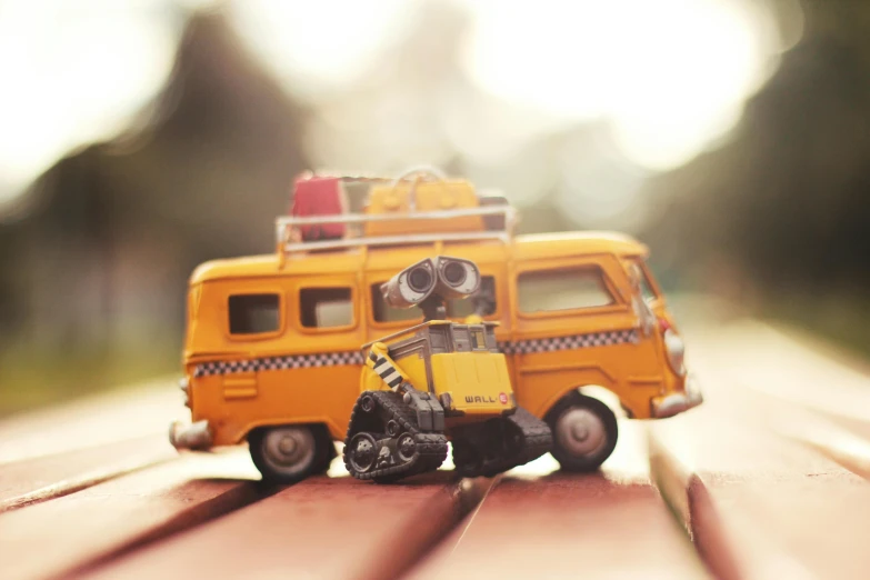 a toy van sitting on top of a wooden table, inspired by Pixar, unsplash, photorealism, buses, yellow, traveller, wall-e