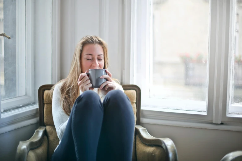 a woman sitting in a chair with a cup of coffee, happening, cosy vibes, grey, uncropped, contented