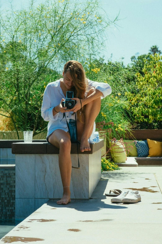 a woman sitting on a ledge with a camera, poolside, jamie chung, in the garden, hasselblad camera