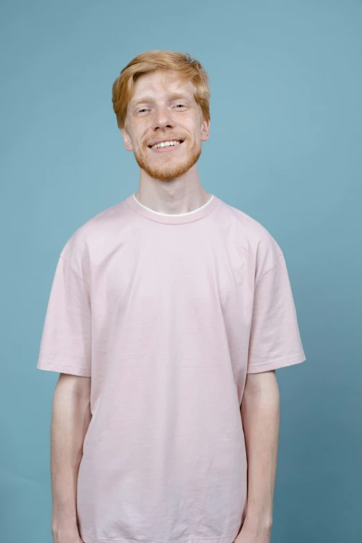 a man standing in front of a blue background, featured on reddit, ginger hair with freckles, pink clothes, on a pale background, like a catalog photograph