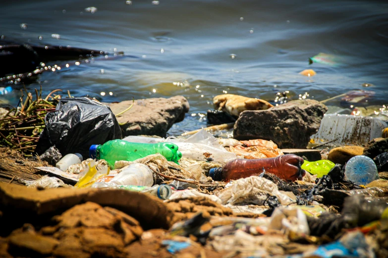 a pile of garbage sitting on top of a beach next to a body of water, water bottles, miscellaneous objects, the world