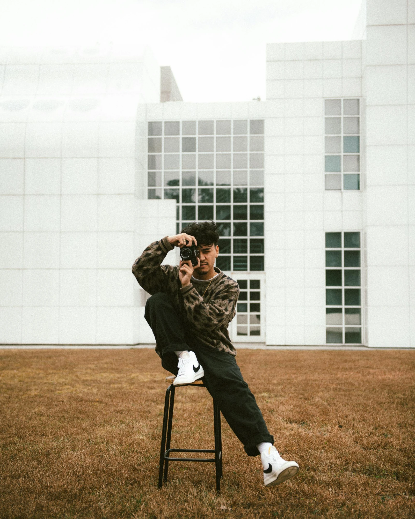 a man sitting on a chair in front of a building, trending on unsplash, visual art, queer woman, wearing camo, asian man, neutral pose