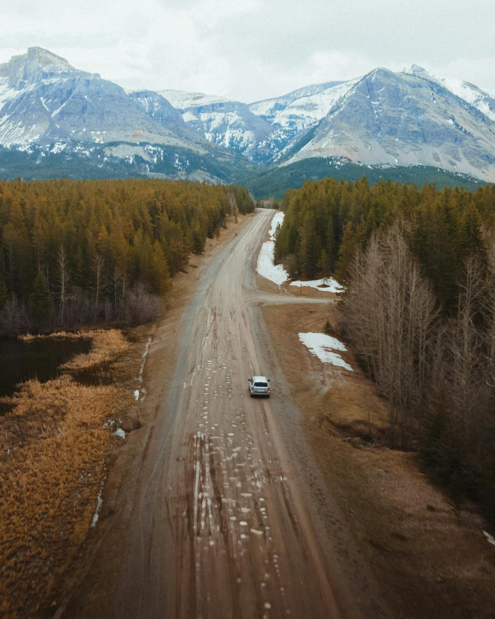 a car driving down a dirt road with mountains in the background, pexels contest winner, boreal forest, birds eye view, winter, conde nast traveler photo