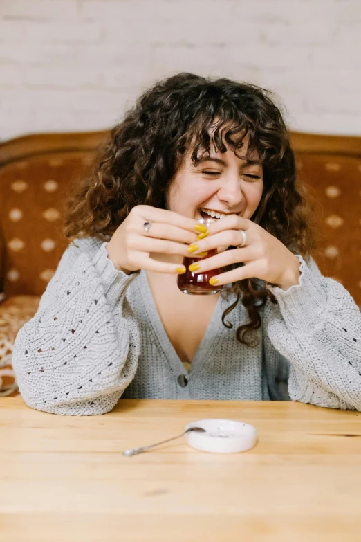 a woman sitting at a table eating a sandwich, pexels contest winner, laughing emoji, drinking cough syrup, curly bangs, sitting with wrists together