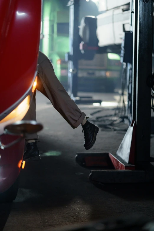 a man sitting on the ground next to a red car, heavy-duty boots, maintenance area, paul barson, getty images