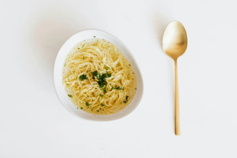 a bowl of noodles and a spoon on a table, white and gold, fan favorite, kailee mandel, soup