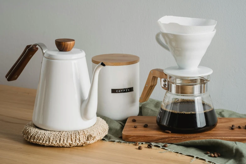 a coffee maker sitting on top of a wooden table, a still life, inspired by Kōno Michisei, trending on pexels, organic ceramic white, from left, cone shaped, zinc white