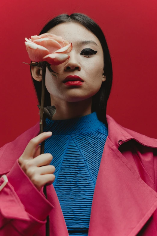 a woman holding a flower in front of her face, an album cover, inspired by Wang E, trending on pexels, red and blue garments, asian descent, fashion portrait, wearing a turtleneck and jacket