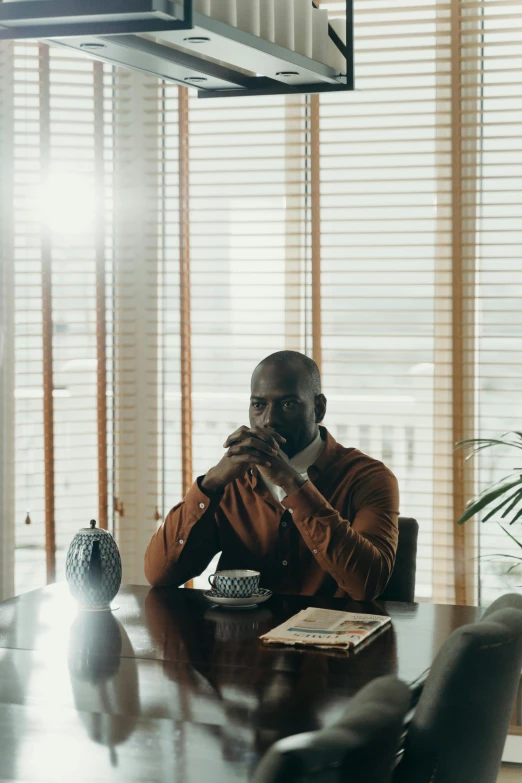 a man sitting at a table talking on a cell phone, an album cover, inspired by Theo Constanté, pexels contest winner, window light, mc ride, in office, sitting on a mocha-colored table