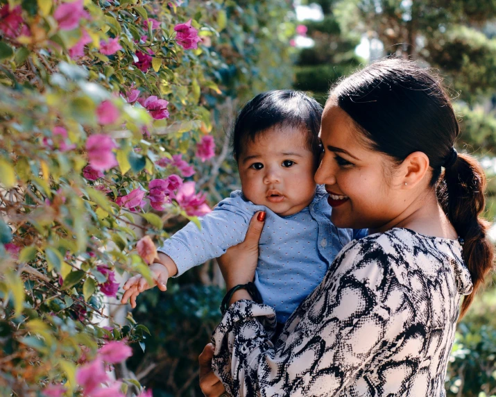 a woman holding a baby in her arms, unsplash, bougainvillea, avatar image, khyzyl saleem, in a garden