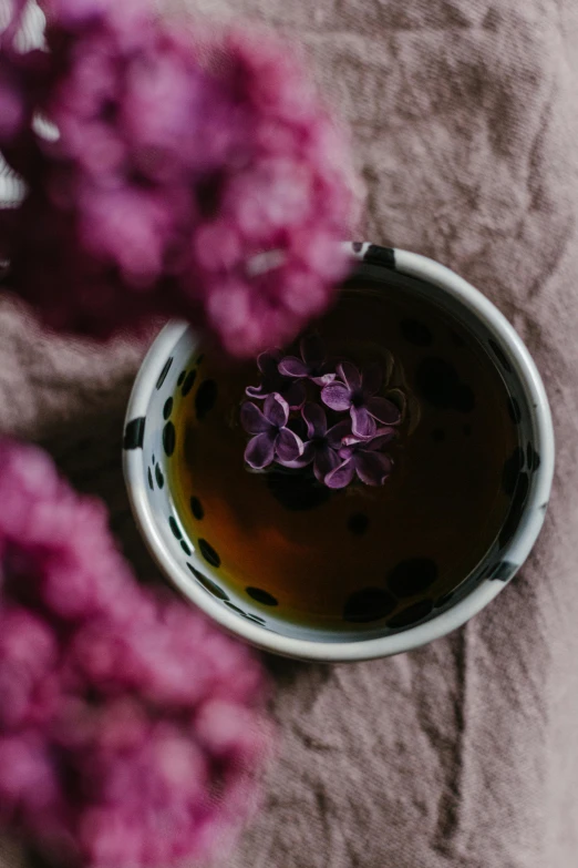 a cup of tea and some purple flowers, a still life, by Lucia Peka, trending on unsplash, black oil bath, high quality photo, dynamic closeup, graphic detail