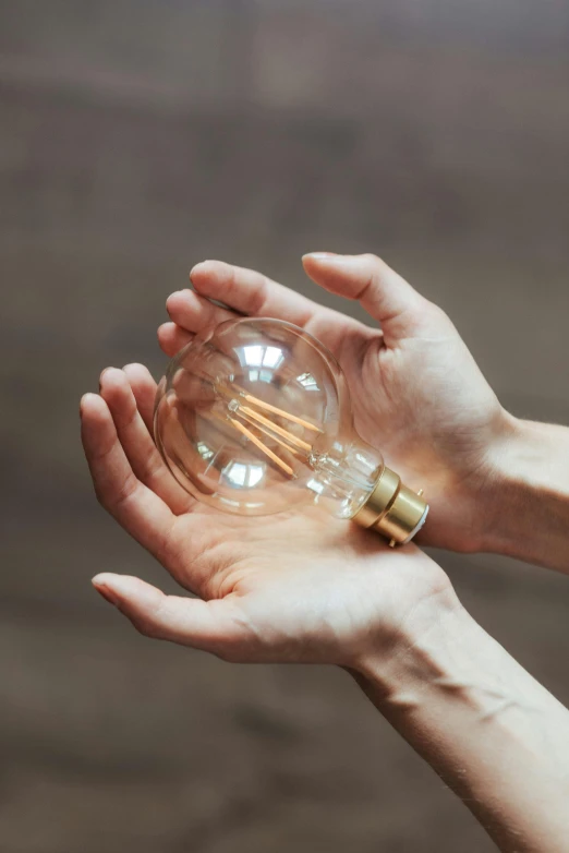 a person holding a light bulb in their hands, sustainable materials, instagram post, very round, gold