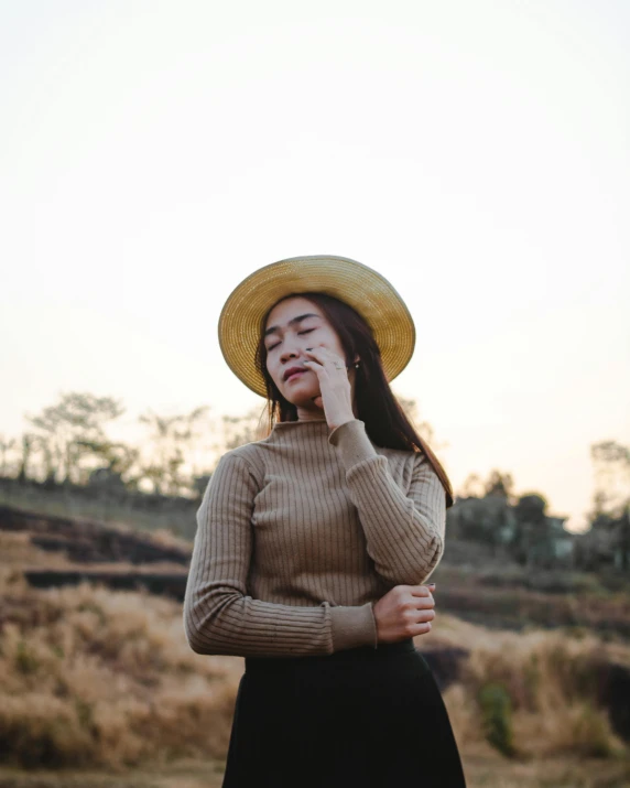 a woman in a hat talking on a cell phone, an album cover, inspired by Ruth Jên, trending on pexels, sumatraism, in the countryside, non binary model, wearing casual sweater, asian women