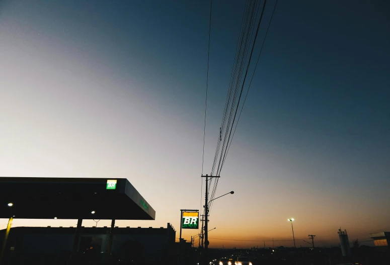 a gas station sitting on the side of a road, an album cover, pexels contest winner, postminimalism, at gentle dawn green light, electrical wires, low quality photo, evening sky