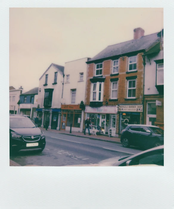 a couple of cars parked on the side of a road, a polaroid photo, unsplash, house's and shops and buildings, wales, medium format, busy small town street