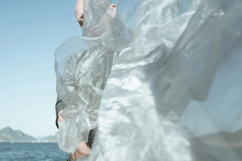 a man standing on top of a boat next to the ocean, an album cover, inspired by Anna Füssli, plasticien, armor made of ice, flowing shimmering fabrics, close-up photograph, ignant