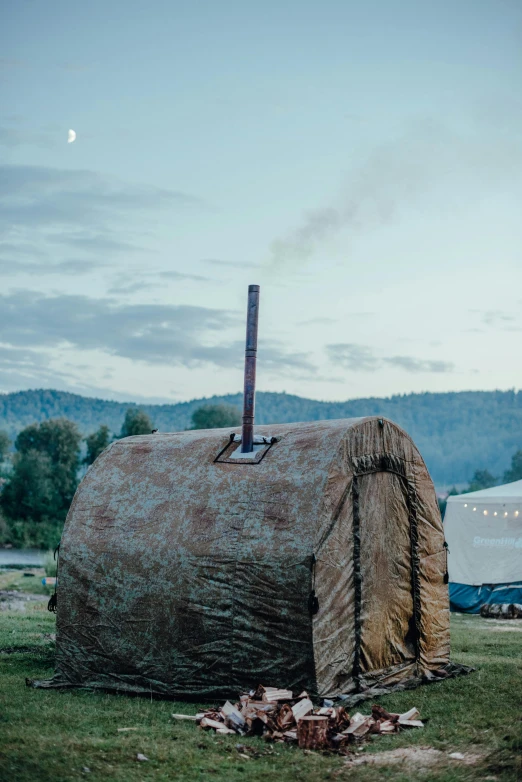 a couple of tents sitting on top of a lush green field, an album cover, inspired by David Ramsay Hay, trending on unsplash, land art, smokestacks, sculpture made of wood, near his barrel home, evening time