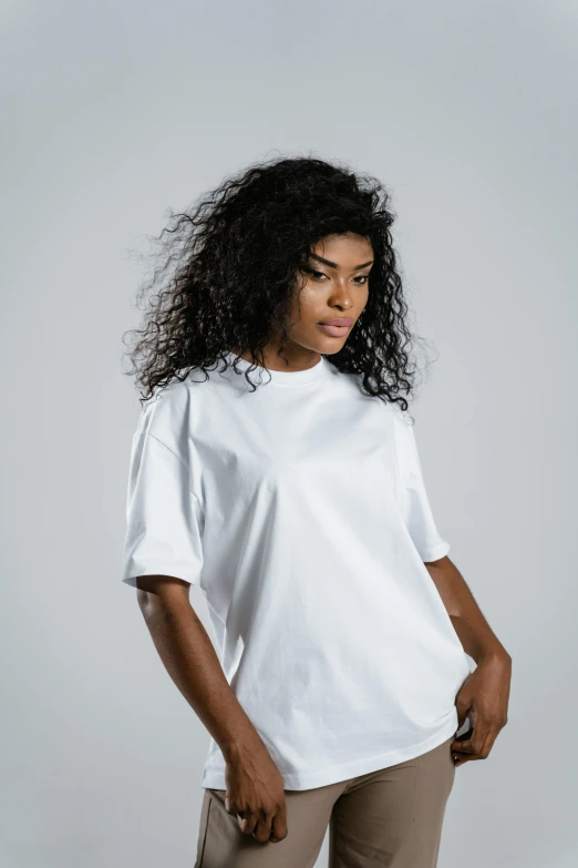 a woman wearing a white t - shirt and khaki pants, an album cover, by Andries Stock, trending on pexels, curls and curves, basic background, sports clothing, white pearlescent