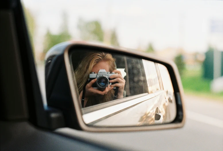 a woman taking a picture of herself in a rear view mirror, a picture, inspired by Vivian Maier, unsplash contest winner, photorealism, f 1.4 kodak portra, full view of a car, back to camera, shot on canon eos r5