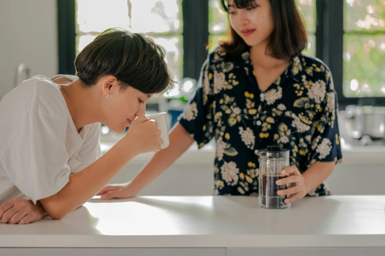 a woman standing next to a boy with a glass of water, pexels contest winner, coughing, hand on table, a young asian woman, lesbian