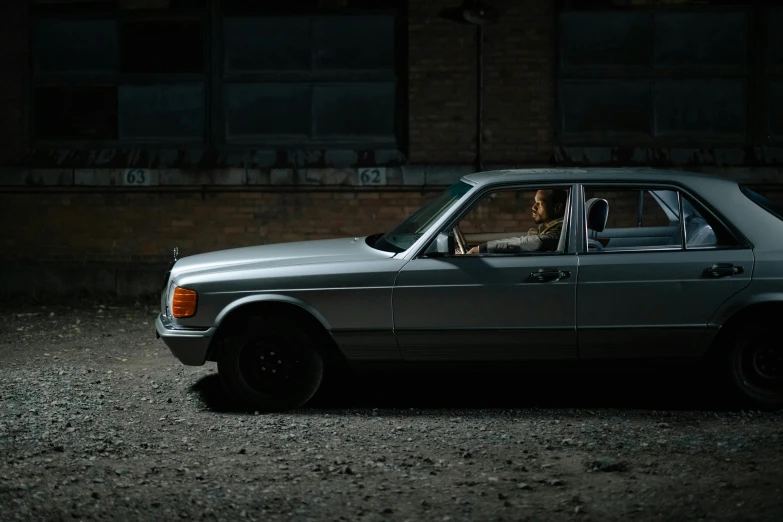 a silver car parked in front of a brick building, an album cover, inspired by Elsa Bleda, pexels contest winner, mercedes, action shot, underexposed grey, 1982