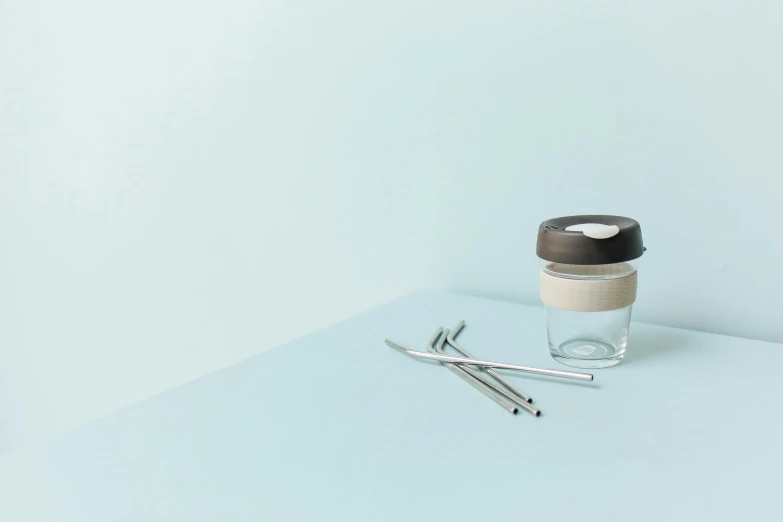 a cup of coffee and a pen on a table, by karlkka, minimalism, surgical implements, inside a glass jar, listing image, pastel blue