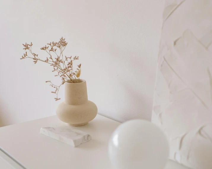 a white table topped with a vase filled with flowers, a marble sculpture, trending on unsplash, minimalism, background image, beige color scheme, product introduction photo