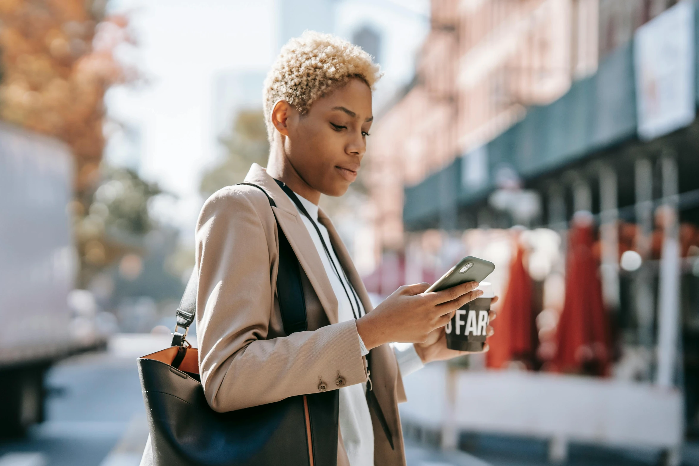 a woman standing on a city street looking at her cell phone, trending on pexels, afrofuturism, corporate phone app icon, short blonde afro, thumbnail, fall season