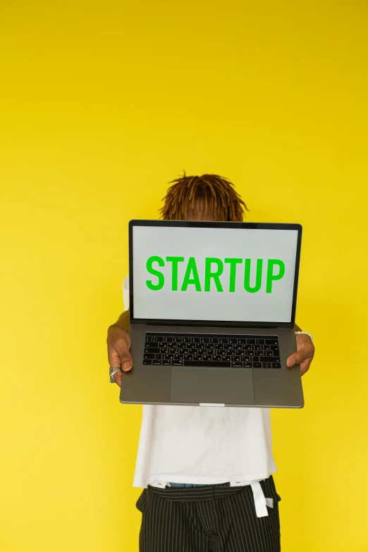 a man holding a laptop with the word start up on it, an album cover, colors: yellow, back - shot, promo image, immature