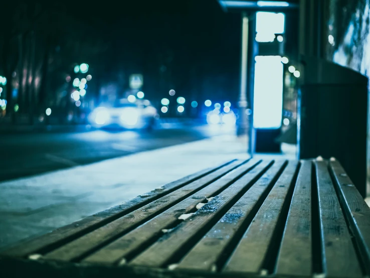 a wooden bench sitting on the side of a street, by Niko Henrichon, unsplash, teal lights, dark city bus stop, homeless, a wooden