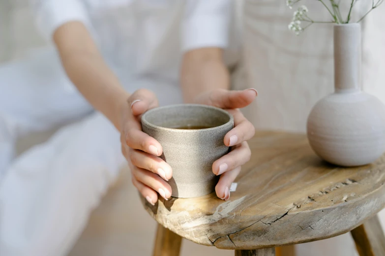 a close up of a person holding a cup on a table, inspired by Kanō Shōsenin, light grey mist, manuka, small, meditative