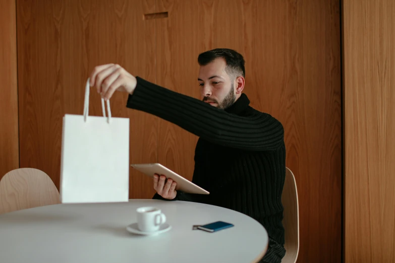 a man sitting at a table with a bag and a tablet, a photo, kacper niepokolczycki, people shopping, high quality image, gif